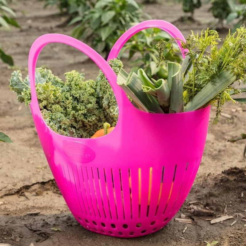 Large pink garden colander basket filled with fresh vegetables in a garden setting